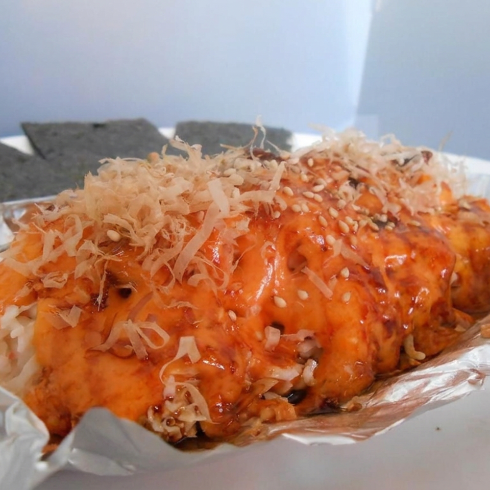 Glazed orange takoyaki topped with bonito flakes and sesame seeds, served in foil with seaweed sheets.