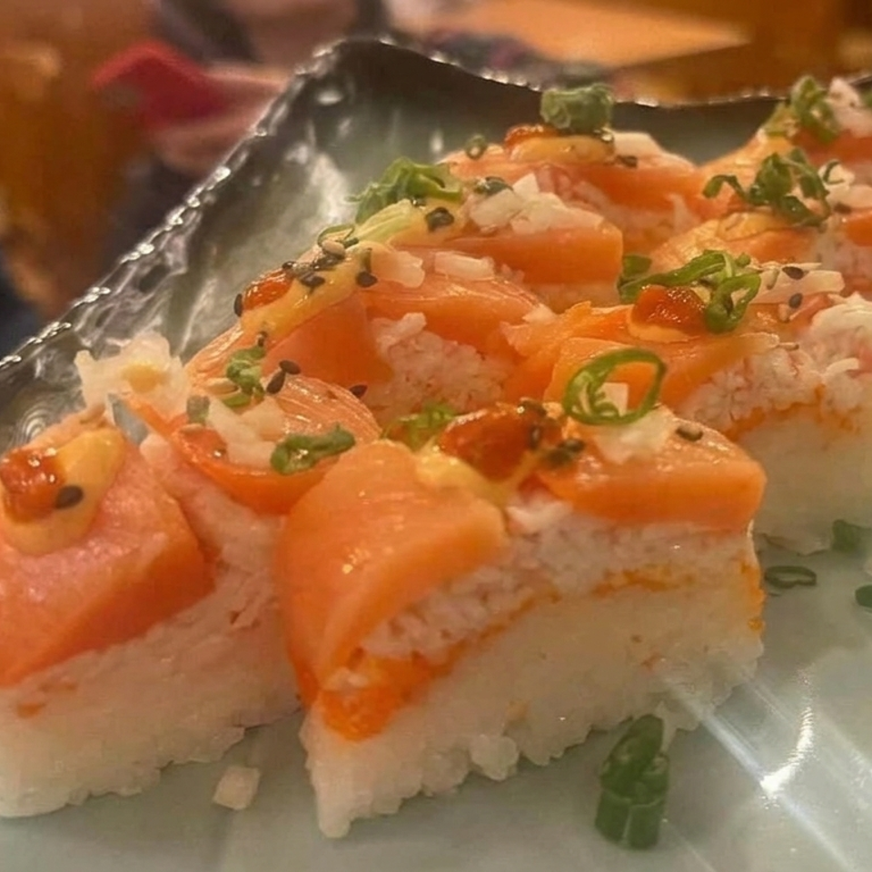 Salmon sushi pieces topped with green onions and sesame seeds arranged on a textured glass plate.