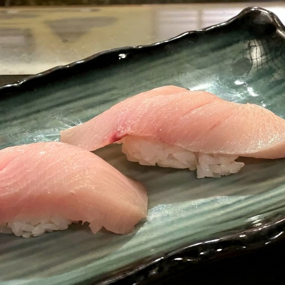 Two pieces of pale pink fish nigiri sushi served on a dark green ceramic plate.