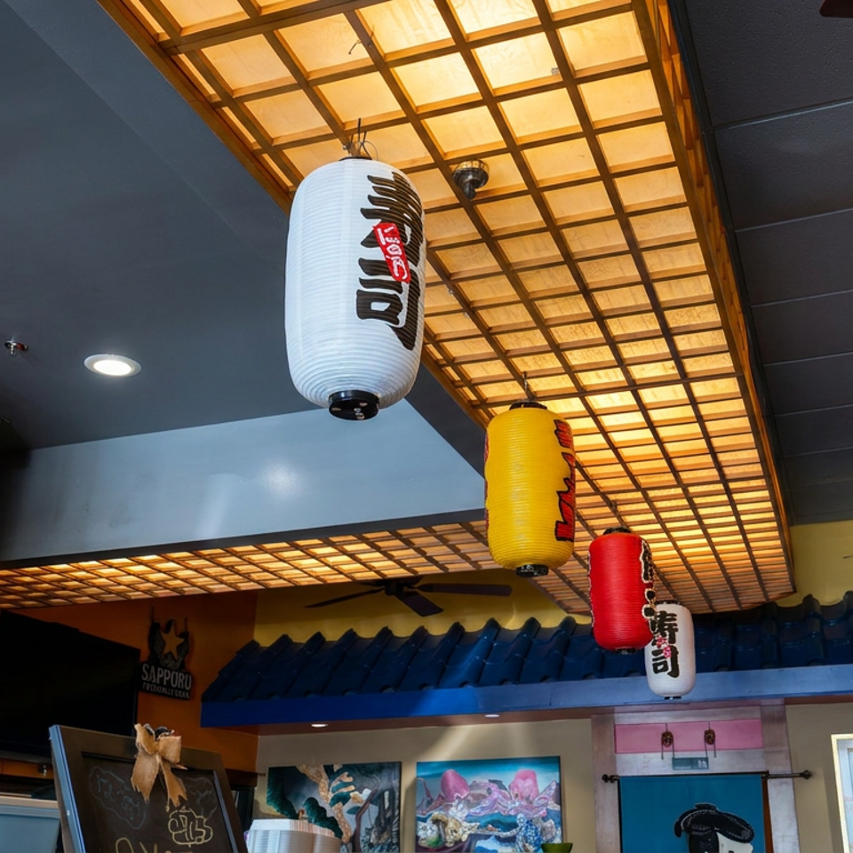 Japanese restaurant interior featuring colorful hanging lanterns, a glowing grid ceiling, blue tiled awning, ceiling fans, and Sapporo décor.