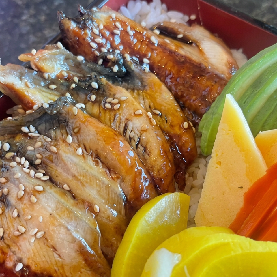Glazed, sesame-topped grilled chicken wings served over rice with avocado, pickled vegetables, and carrot slices.