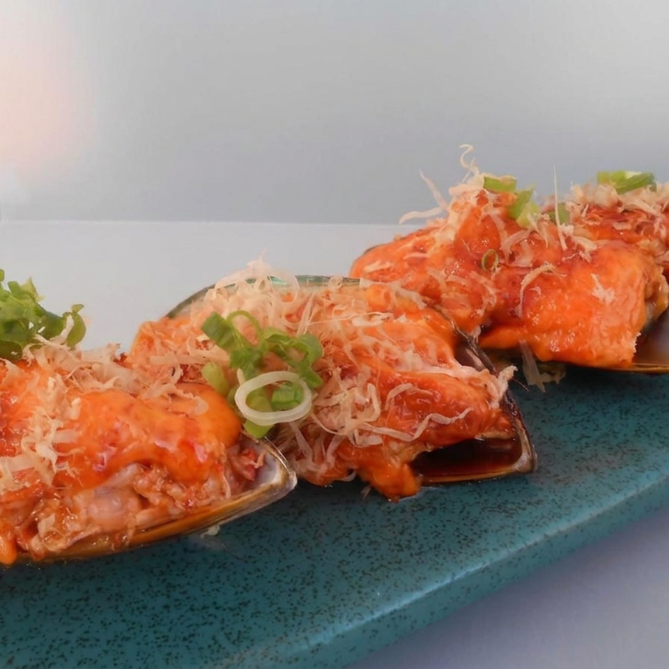 Orange-glazed mussels topped with shredded garnish and green onions arranged on a rectangular blue serving plate.