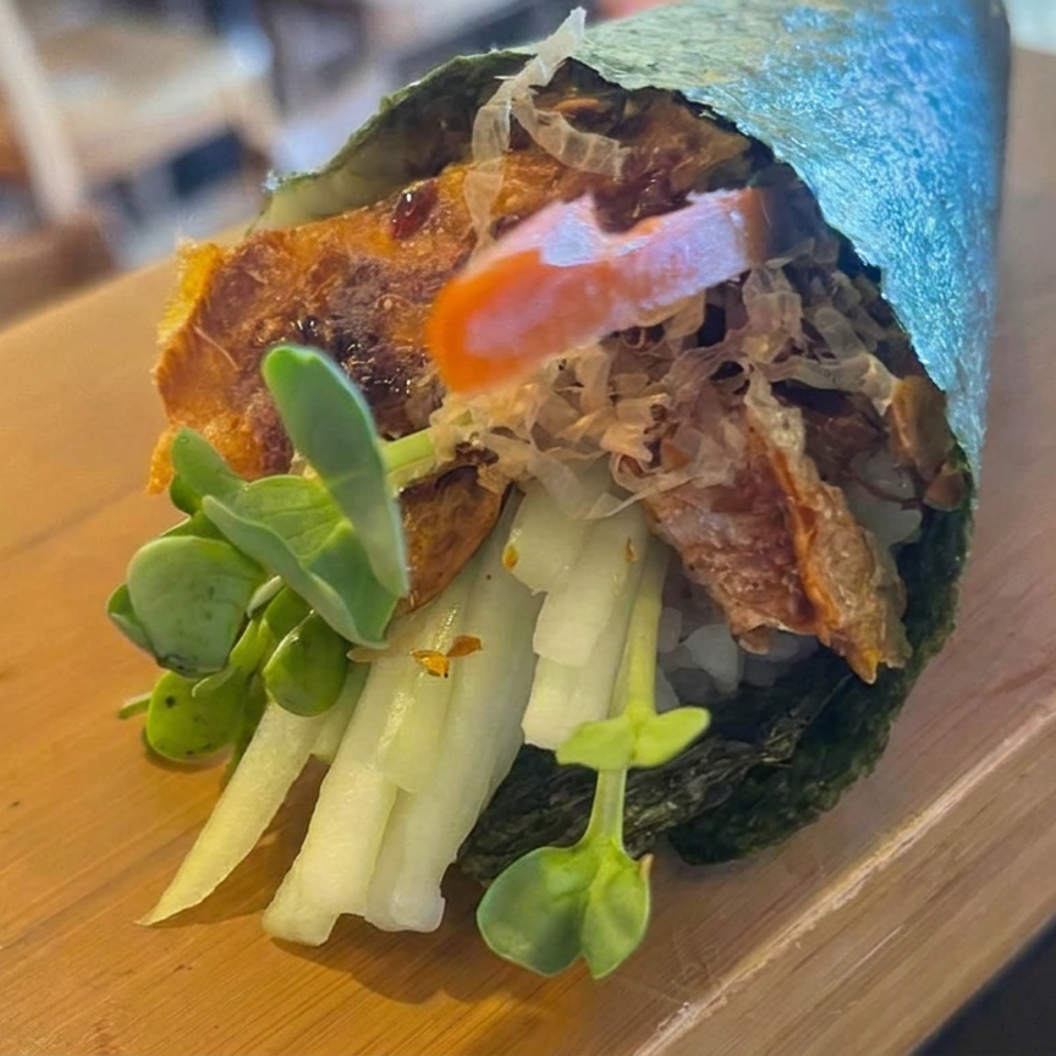 Open-faced seaweed taco topped with crispy filling, shredded cabbage, tomato, cucumber, and fresh greens on a wooden table.